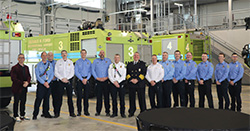 Airport staff and fire department personnel posing for a group photo in front of fire trucks
