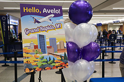"Hello, Avelo, Grand Rapids, MI" welcome sign with purple and white balloons at an airport gate