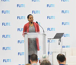 Woman speaking at a podium in front of a FLITE branded step-and-repeat backdrop