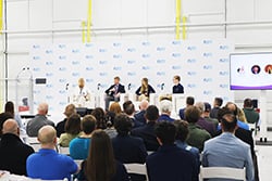 Three attendees in business attire talking near a reception table at an event