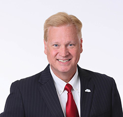 Professional headshot portrait of Dan Koorndyk in a suit and red tie