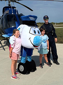 Two children posing with the Jerry the Jet mascot and a police officer in front of a helicopter