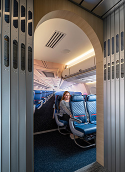 Woman seated in an airplane cabin mock-up, viewed through an accordion door