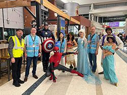 Group photo of airport staff with costumed superhero and princess characters