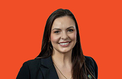 Professional headshot portrait of a woman in a blazer against an orange background